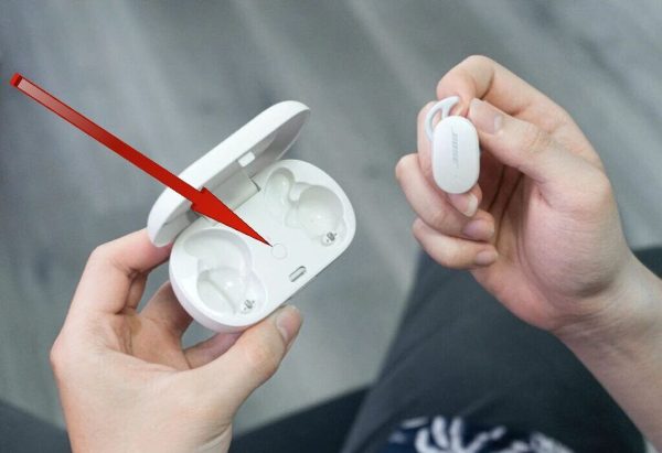 A red arrow pointing towards Bluetooth buttons of Bose earbuds held in a girls hand