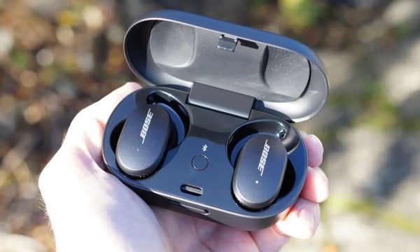 A man's hand holding Bose Earbuds case with earbuds inside, in sunlight