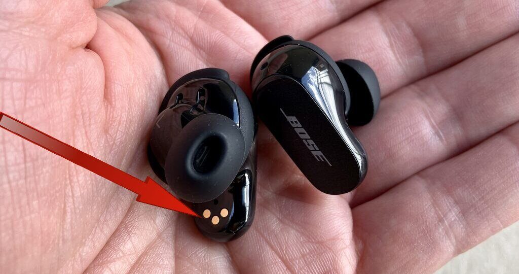 A red arrow pointing towards charging contacts of Bose QuietComfort present in a person's hand 