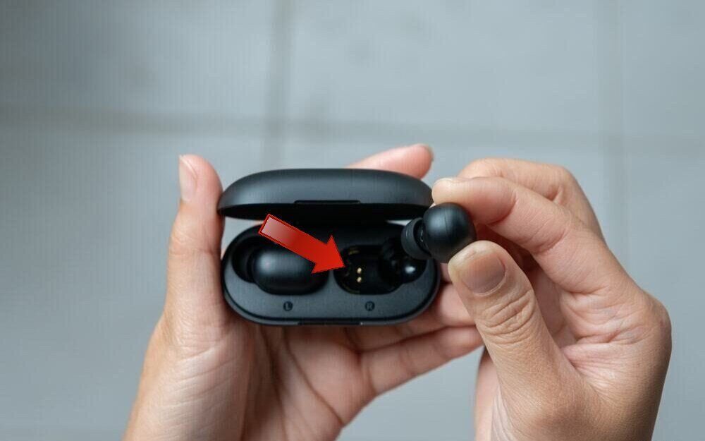 A girl's hand holding Indy Evo earbuds and a red arrow pointing towards the charging contacts 