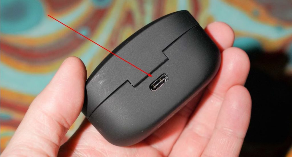 Red arrow pointing towards charging port of a earbuds case that a person is holding