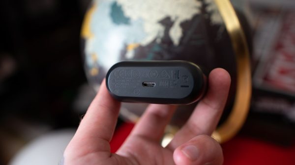 A man holding a Skullcandy earbud reveals its underside, showcasing the charging port